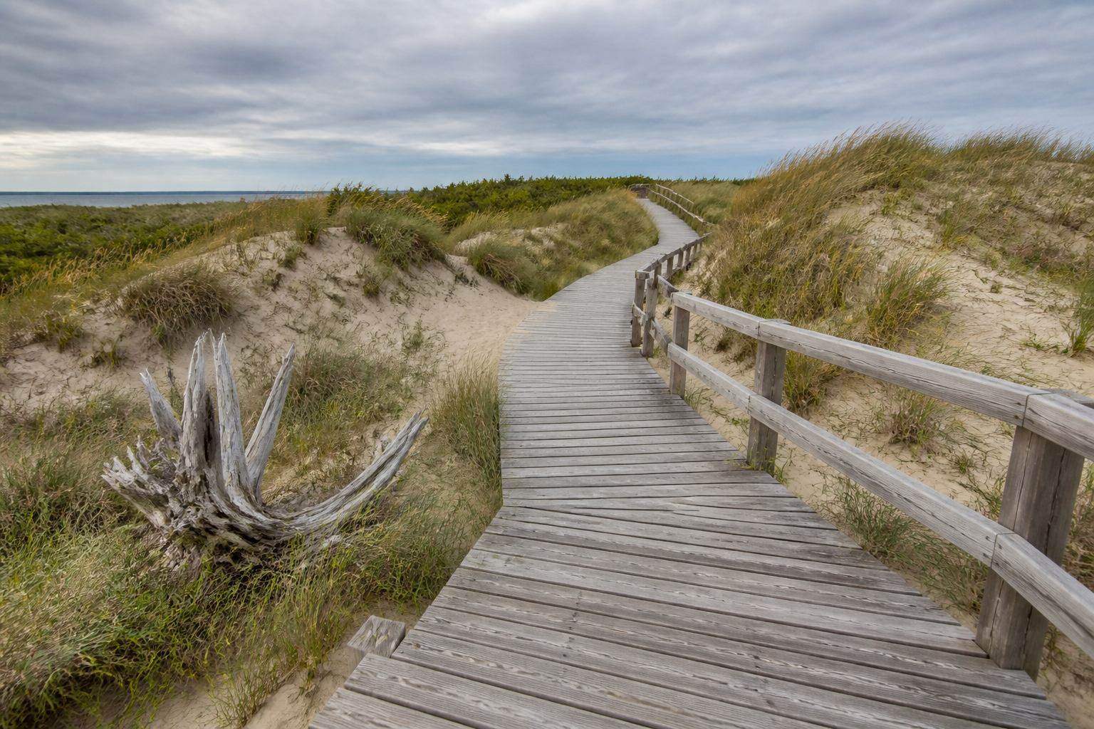 Holzsteg über Dünengras und Sandrücken Richtung Ostsee